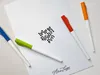 Four colored pens are arranged on a white sheet of paper with calligraphy text and a signature. Voir les images du produit