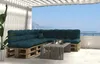 A modern outdoor lounge area with a sectional sofa made from pallets and dark green cushions, a wooden coffee table, and a view of the sea and mountains. Voir les images du produit