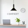 A modern office reception area with a laptop, plant, and clock on a desk, under a pendant lamp. Produktbild-Vorschau