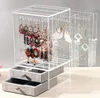 A clear acrylic jewelry organizer box with multiple tiers and drawers, filled with various earrings. Voir les images du produit