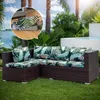 An outdoor sectional sofa with tropical-themed cushions is placed on a lawn next to a pool, with palm trees and water in the background. An inset shows a close-up of a cushion cover being put on. Náhled obrázku produktu