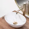 A close-up shot of a marble-patterned vessel sink with a gold faucet, placed on a wooden surface. Produktbild-Vorschau
