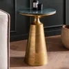 A close-up shot of a round marble-top side table with a gold metal base, placed next to a sofa in a room with dark green paneled walls and a wooden floor. Produktbild-Vorschau