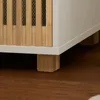 A close-up view of the bottom corner of a white cabinet with wooden slatted detailing and wooden block feet, resting on a brown wooden floor. Voir les images du produit