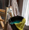A close-up of a black bucket with blue liquid and a yellow cloth hanging on a wooden ladder. Produktbild-Vorschau