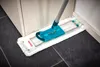 A mop with a white microfiber head and turquoise handle is cleaning a dark tiled floor next to a white cabinet. Produktbild-Vorschau