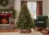 A Christmas tree decorated with pine cones and lights, standing next to a fireplace with stockings hung on it, and a green armchair in a living room. Voir les images du produit