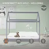 A children's wooden cot in a light grey color, with a mattress and a teddy bear on it. There are decorative pictures on the wall behind the cot. Náhled obrázku produktu