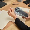 A person is using a DYMO label maker to label a file folder on a desk. Produktbild-Vorschau