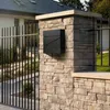 A modern black mailbox is mounted on a stone pillar next to a metal fence, with a house in the background. Produktbild-Vorschau