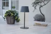 A gray table lamp sits on an outdoor table next to a basket of greenery and a notebook with a pen. Produktbild-Vorschau