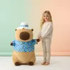 A young girl holding hands with a large capybara plush toy. Produktbild-Vorschau
