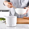 A person is holding a wooden utensil and a white bowl over another white bowl. Produktbild-Vorschau