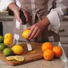 A person is zesting a lemon over a cutting board with other citrus fruits. Anteprima dell’immagine prodotto