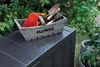 A wooden garden box filled with gardening tools sits on top of a dark gray storage box outdoors, with lush green foliage in the background. Anteprima dell’immagine prodotto