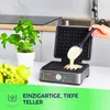 A waffle iron is being used to make waffles, with fruit and a plant in the background. Náhľad obrázku produktu
