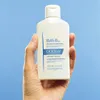 A hand holding a bottle of shampoo against a blue background. Produktbild-Vorschau