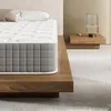 A close-up view of a mattress on a wooden bed frame, with a bedside table and lamp in the background. Produktbild-Vorschau