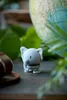 A small, grey elephant figurine is placed on a surface in front of a globe and green foliage. Produktbild-Vorschau