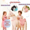 Two young girls interacting with a plush unicorn toy, with inset images showing a black horse toy and a girl on a white unicorn toy. Produktbild-Vorschau