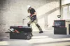 A construction worker is using a drill on a wall, with toolboxes nearby. Náhled obrázku produktu