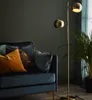 A modern living room scene with a dark sofa, decorative pillows, and a brass floor lamp. Produktbild-Vorschau