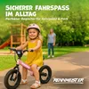 A young girl is riding a pink balance bike in a park, with a playground and trees in the background. Produktbild-Vorschau