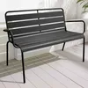 A dark gray metal garden bench sits on a light-colored wooden deck, with shadows cast by palm fronds on the wall behind it. Produktbild-Vorschau