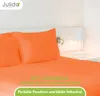 A close-up view of orange bedding, including pillows and a fitted sheet, on a bed with a white headboard and a bedside lamp. Produktbild-Vorschau