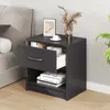 A dark gray nightstand with an open drawer is placed next to a bed in a bedroom setting. The nightstand has books and a cup on it, and a plant is visible in the background. Podgląd zdjęcia produktu