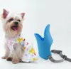 A small dog wearing a dress sits next to a blue dog muzzle. Produktbild-Vorschau