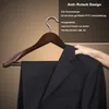 A dark suit jacket and pants hanging on a wooden hanger, with a hand adjusting the jacket shoulder. Produktbild-Vorschau