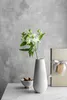 A white vase with flowers, cookies in a bowl, and a gift box on a marble surface against a concrete wall. Produktbild-Vorschau