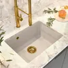 A beige under-mount sink with a gold faucet and drain, set on a marble countertop. Podgląd zdjęcia produktu