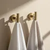 Two gold bathroom hooks on a light-colored wall, each holding a towel. Produktbild-Vorschau