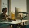 A man is working at a desk with a computer monitor on a stand. Produktbild-Vorschau