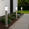 Three modern stainless steel bollard lights illuminate a pathway next to a white house with green landscaping. Náhľad obrázku produktu