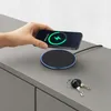 A hand is placing a smartphone onto a black wireless charging pad on a gray surface. A set of keys is also on the surface. Produktbild-Vorschau