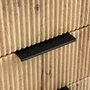A close-up view of a wooden dresser or cabinet with ribbed texture and black drawer pulls. Produktbild-Vorschau