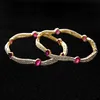 A pair of gold bangles with pink stones and diamond-like accents against a black background. Produktbild-Vorschau