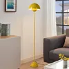 A yellow floor lamp is shown in a living room setting next to a sofa and a cabinet. Produktbild-Vorschau