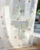 A sheer curtain with pompom details is draped over a window, with a vase of greenery visible behind it. Produktbild-Vorschau