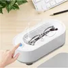 A hand is pressing a button on a white ultrasonic cleaner with glasses inside, with water splashing. Voir les images du produit