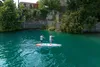 Two people paddleboarding on a clear turquoise lake with a stone wall and building in the background. Voir les images du produit