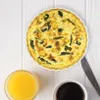 A quiche with spinach and possibly salmon, served with orange juice and coffee on a white wooden table. Produktbild-Vorschau