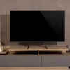A modern TV stand with a black television on top, set against a textured brown wall. Náhled obrázku produktu