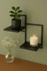 A black metal wall shelf with a potted plant and a lit candle. Produktbild-Vorschau