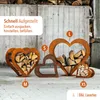Several heart-shaped metal wood racks filled with firewood are displayed on a paved surface in front of a wooden wall. Produktbild-Vorschau