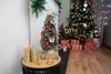A small decorated Christmas tree sits on a table next to a fireplace, with a larger Christmas tree and gifts in the background. Voir les images du produit