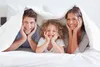 A family of three is lying in bed under a duvet, smiling at the camera. Produktbild-Vorschau